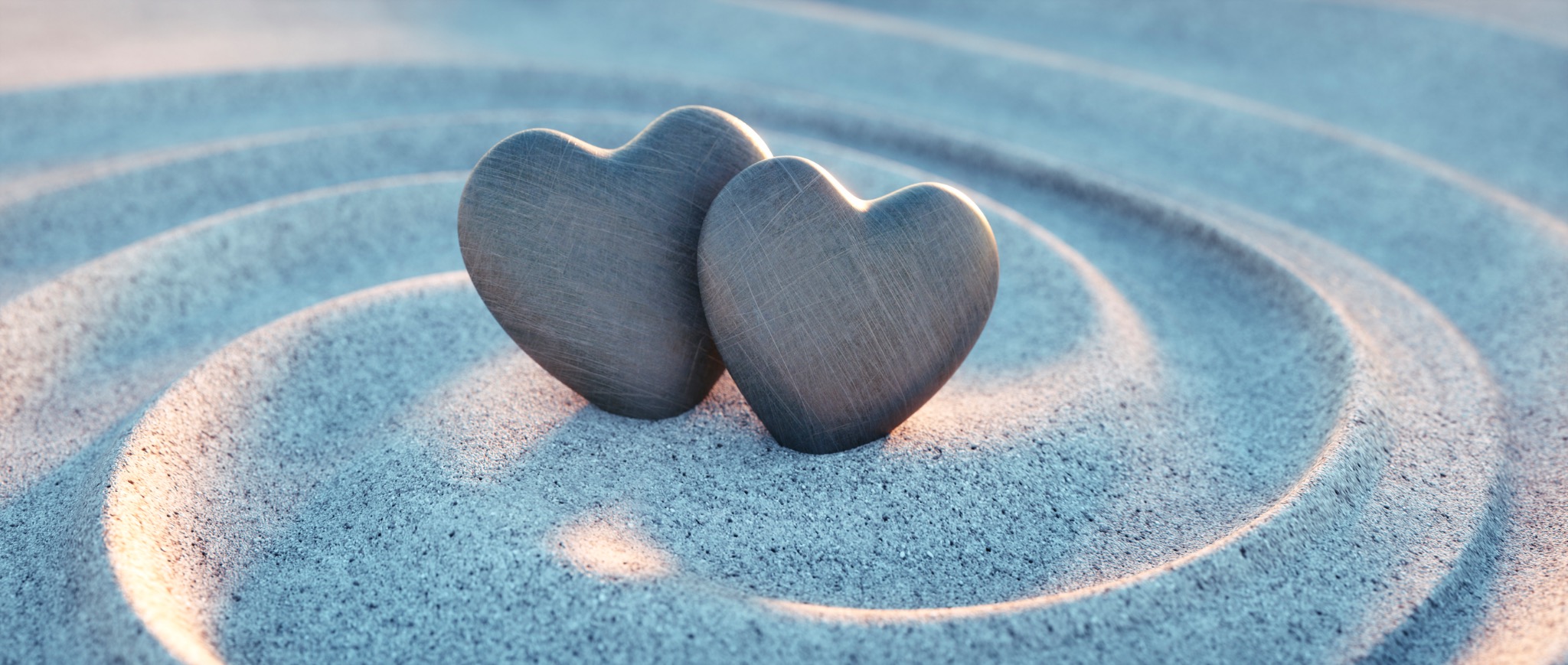 Two heart-shaped stones resting together within concentric circles in the sand